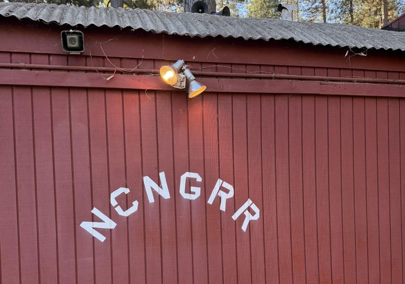 Red board-and-batten wall of the hut with NCNGRR stenciled in white letters under a corrugated roof edge.