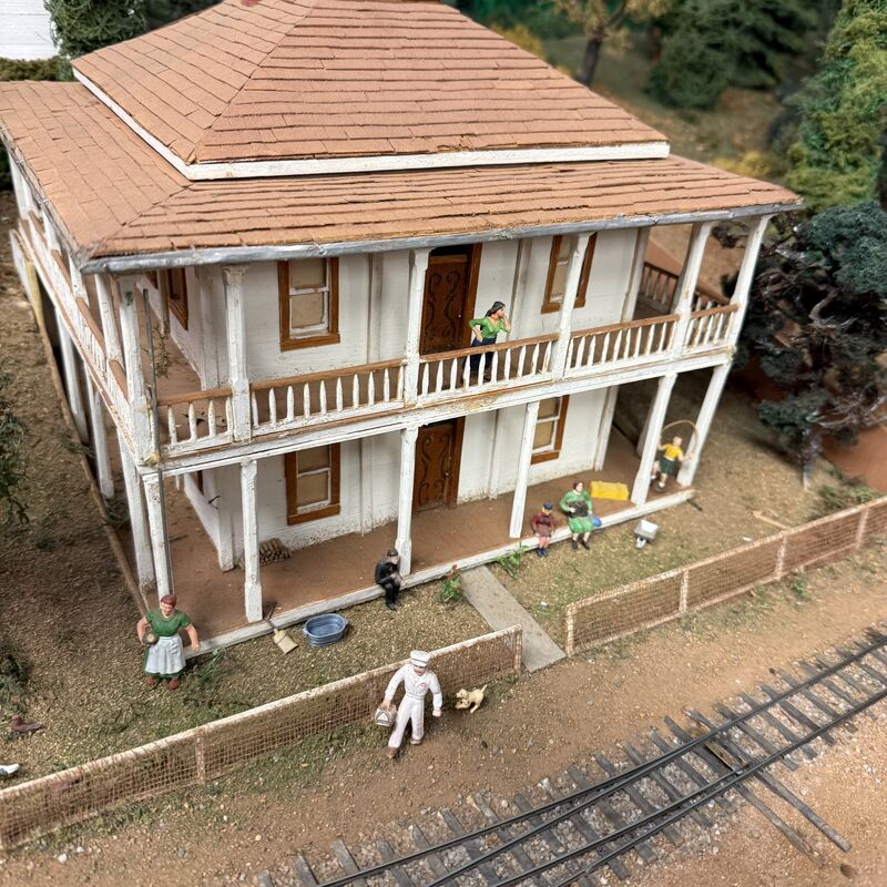 Two-story model house with wraparound porches and figures in the yard