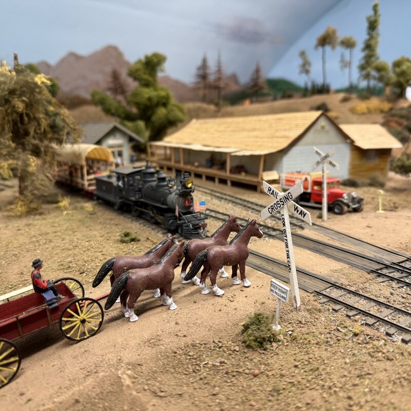Horse-drawn wagon at a crossing beside a steam locomotive and depot