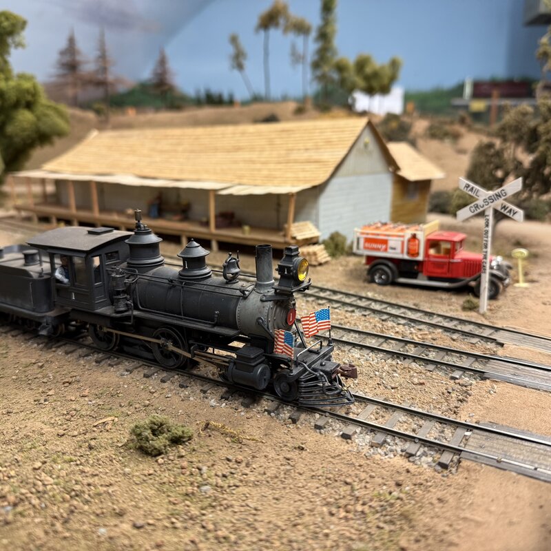 Side view of a steam locomotive and tender at a railroad crossing