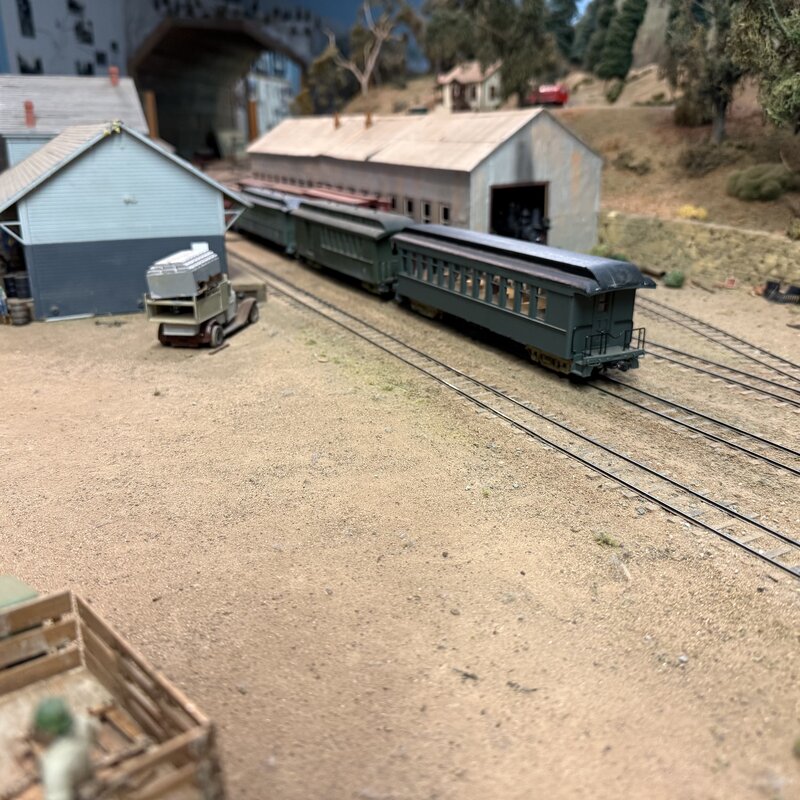 Green passenger coaches beside railroad workshop buildings