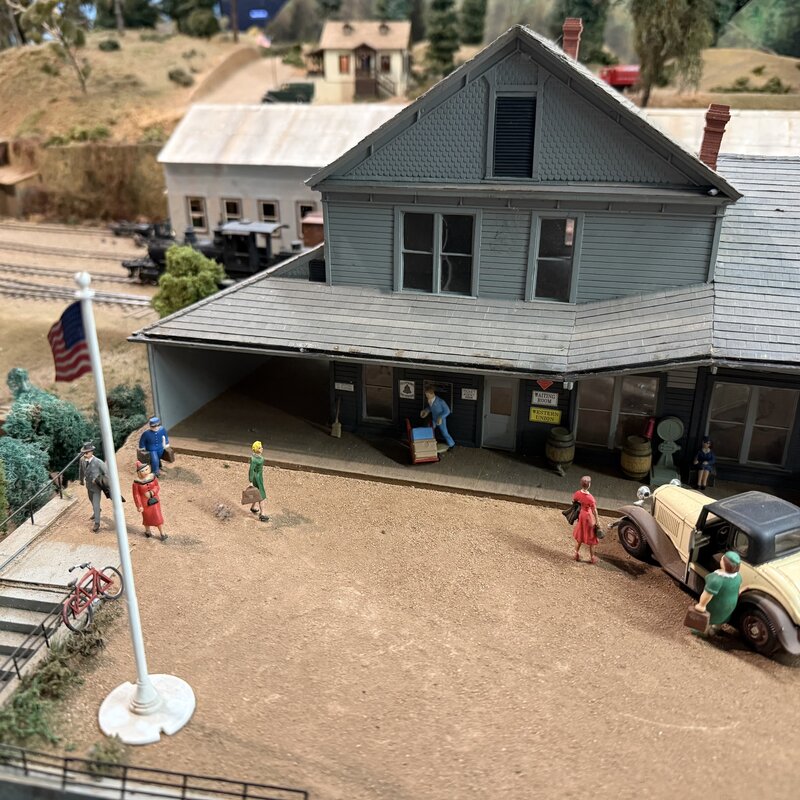 Two-story depot with miniature figures, vintage cars, and a flagpole