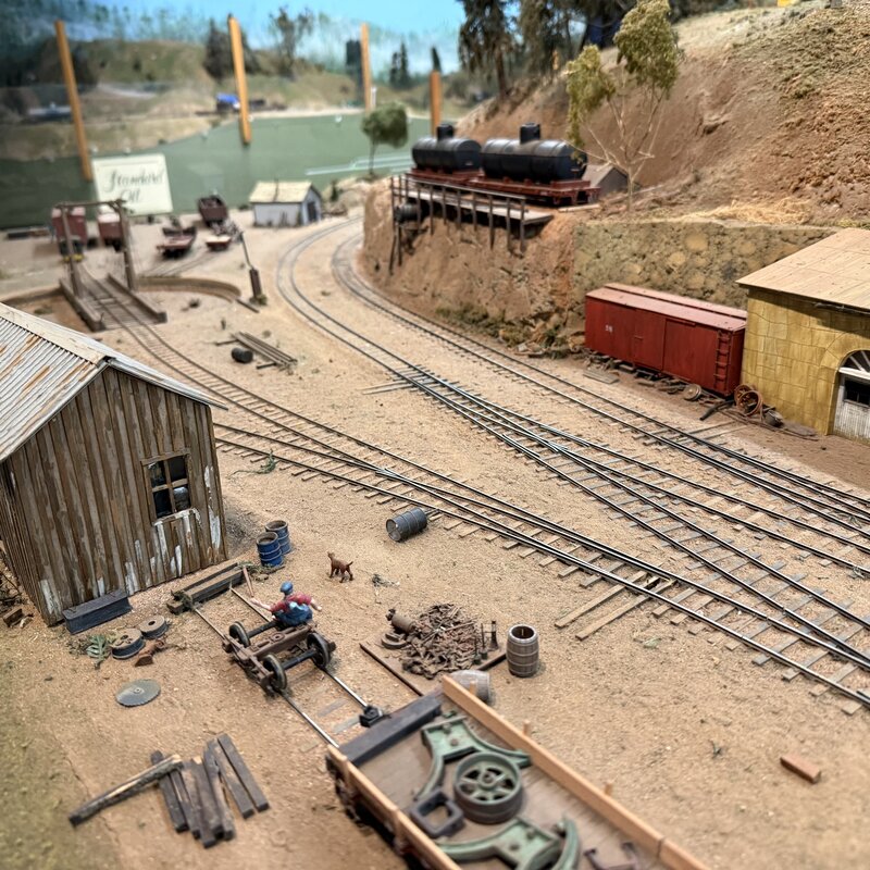 Railroad maintenance yard with machinery, sidings, and hillside storage tanks