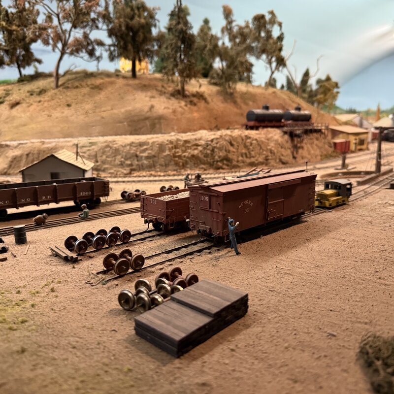 Freight car repair scene with spare wheelsets and stacked lumber