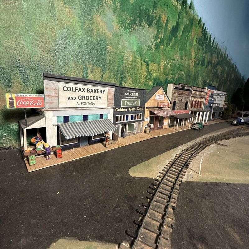 Model storefronts along a street beside a curved railroad track