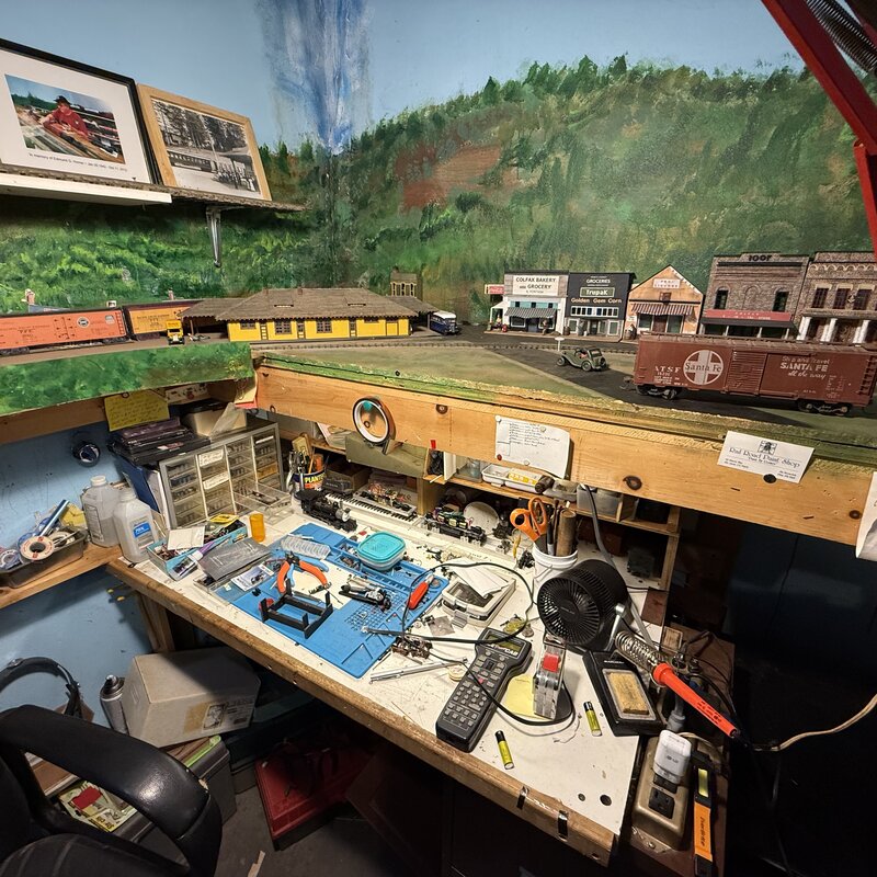 Model railroad workbench with tools and locomotives beneath the town scene