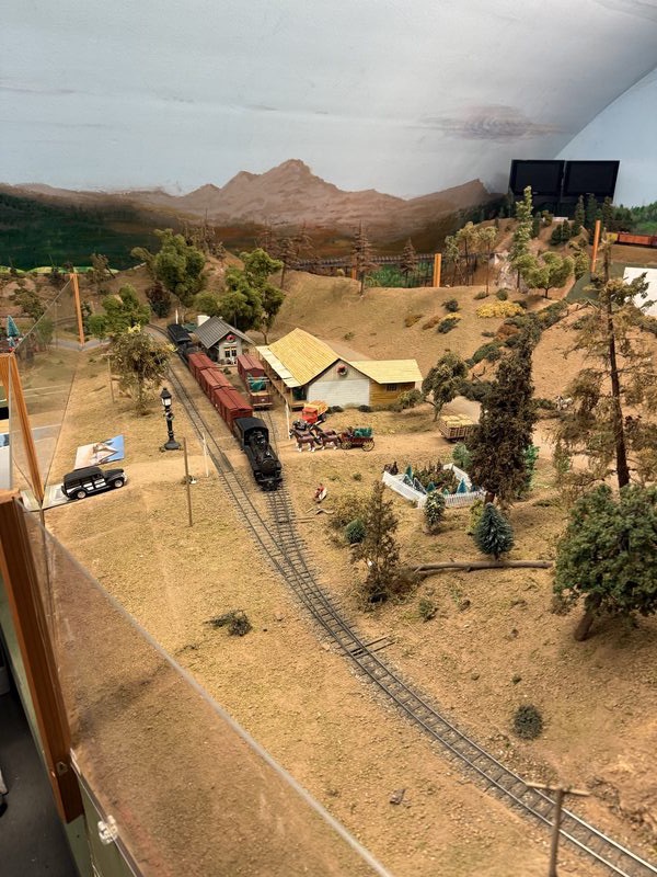 Steam locomotive passing through town with buildings and Sierra backdrop